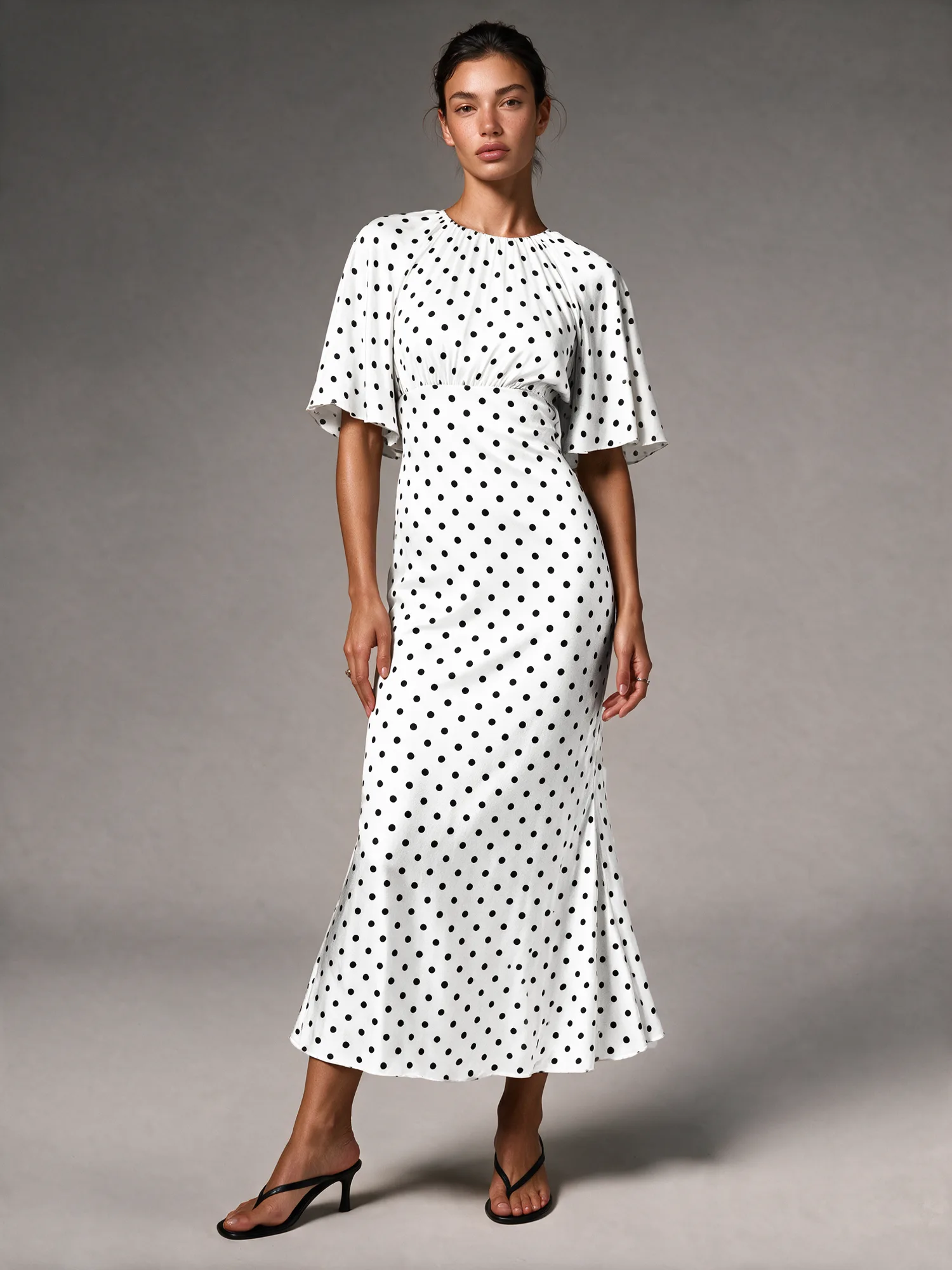 Model wearing a white polka-dot dress in a gray studio