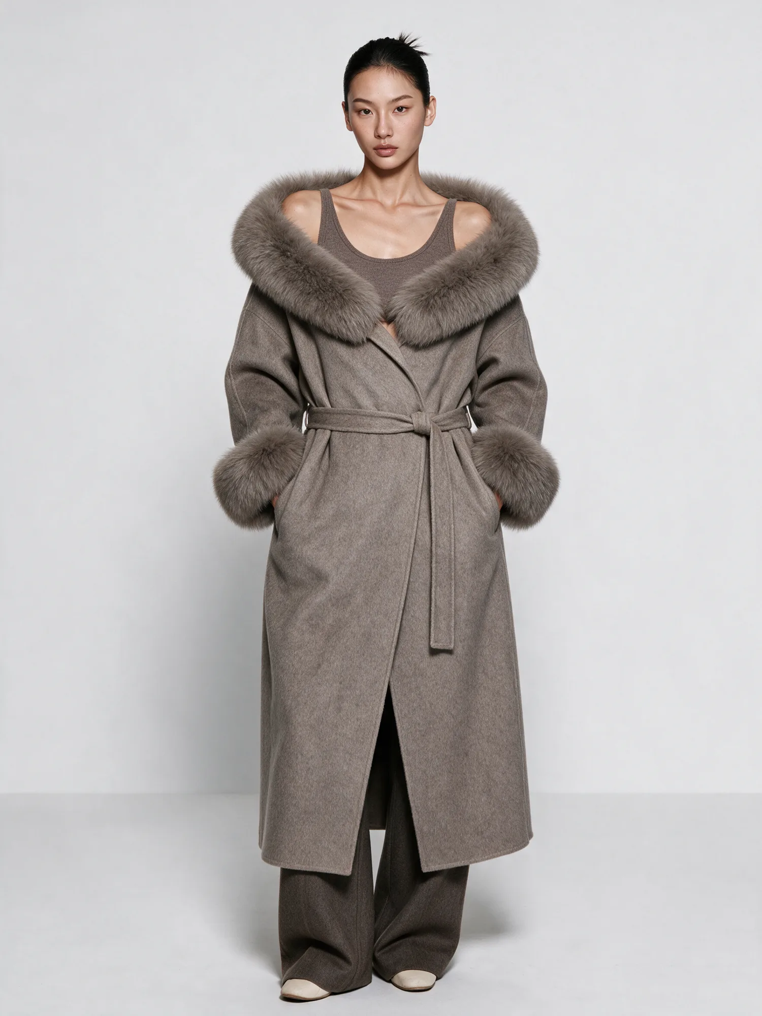 Studio model image showing a long gray coat with fur trim
