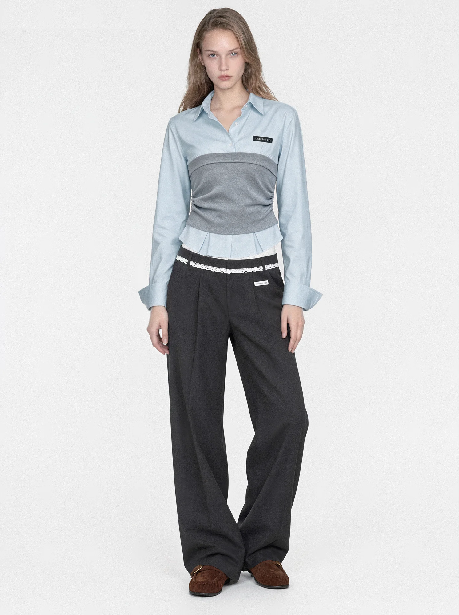 Full-length model wearing a pale blue shirt with a gray waist panel, black wide-leg trousers and brown shoes on a white background