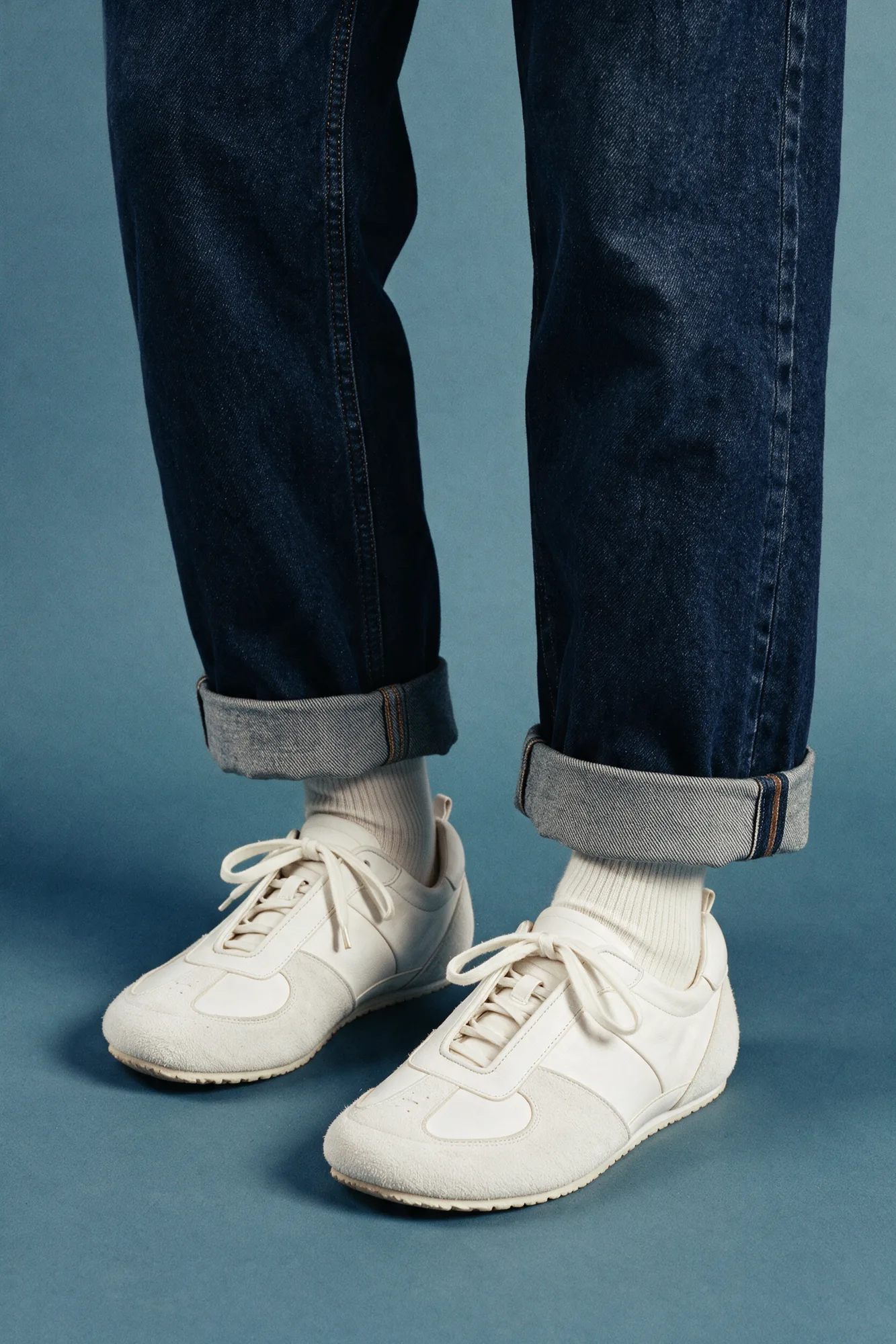 White trainers styled with rolled denim on a blue studio floor